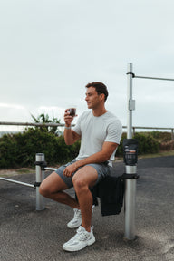 A person sitting on a bench outdoors holding a protein coffee